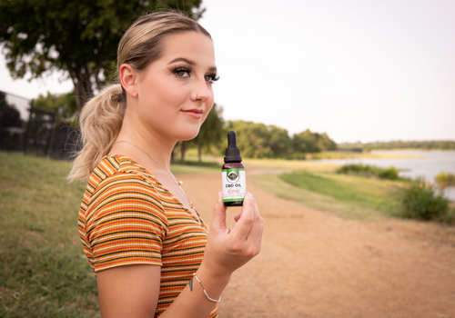 Young woman outdoors holding up a cbd oil tincture and smiling