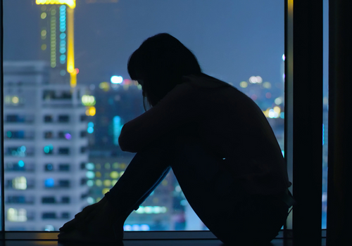 Silhouette of depressed man sitting in window with cityscape behind him